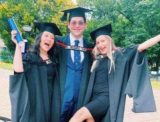 Three Swiss Hotel School graduates celebrating in their gowns and caps